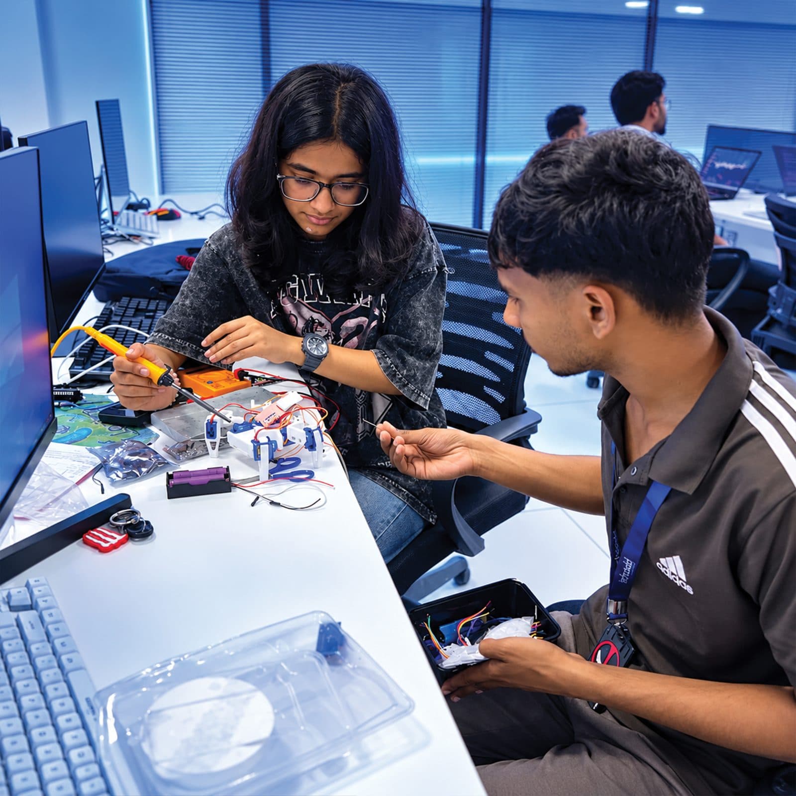 Student soldering a robotics kit while a mentor helps